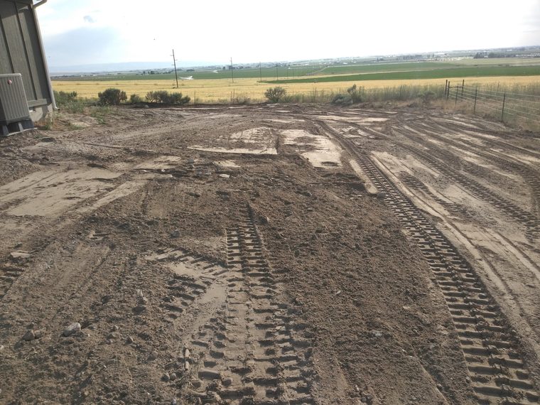 Freshly graded dirt lot with excavator track marks next to a house