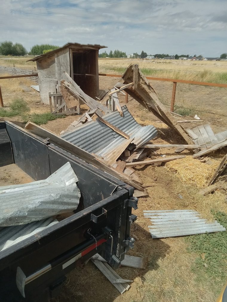 Corrugated metal and old lumber from a torn-down shed being loaded into a black dump trailer